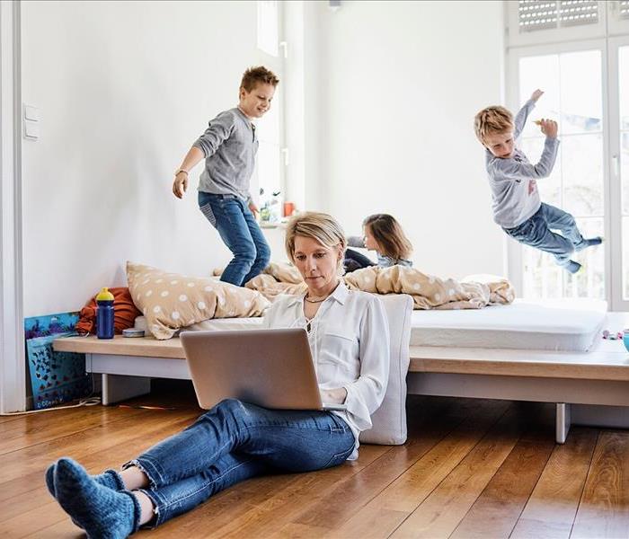 Woman working on laptop in bedroom with children jumping on the bed 